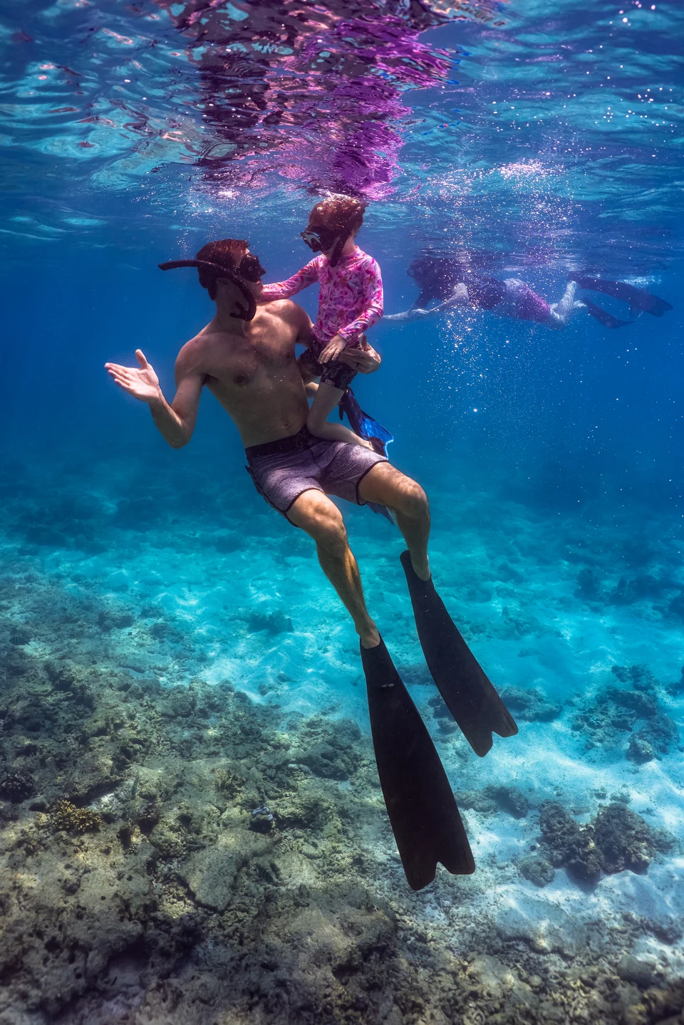 A father and daughter snorkeling together above the reef.